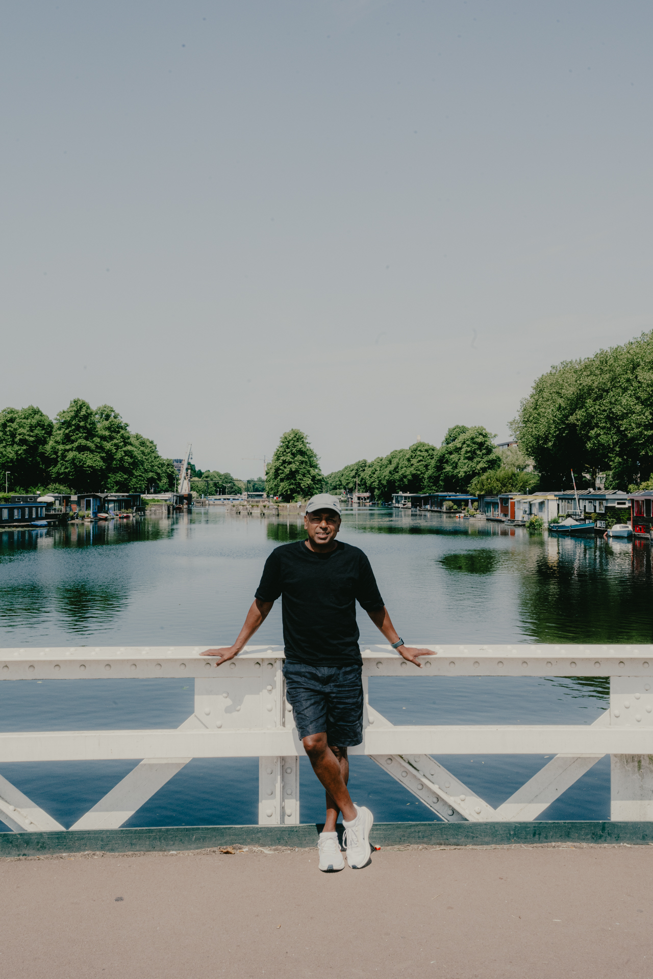 A photo of Ramdath. He is standing on a bridge, leaning against the railing. In the background, you can see water with houseboats along the docks.